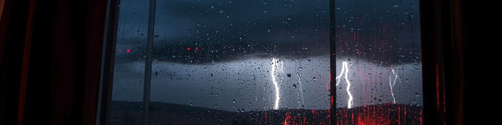 Vista noturna de uma paisagem com chuva intensa e relâmpagos (raios) através de uma janela molhada.