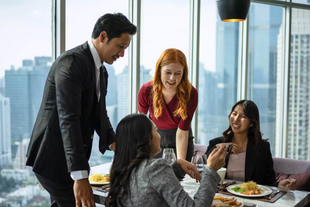 Um grupo diversificado de quatro profissionais em trajes de negócios celebra em um restaurante de luxo com vista para a cidade.