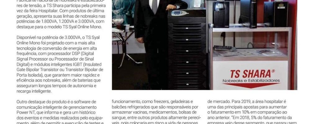 Homem de terno ao lado de nobreaks expostos no estande da TS Shara durante a feira Hospitalar, com painel da marca ao fundo.