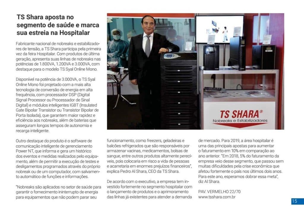 Homem de terno ao lado de nobreaks expostos no estande da TS Shara durante a feira Hospitalar, com painel da marca ao fundo.