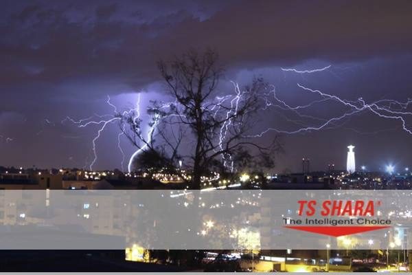 Vista noturna de uma cidade com relâmpagos no céu e o logotipo da TS Shara em destaque na parte inferior.