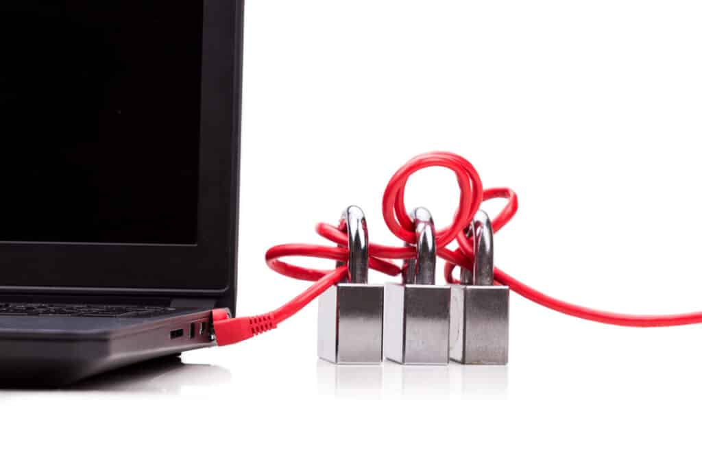 Um cabo de rede vermelho, plugado na lateral de um notebook preto, está emaranhado em volta de três cadeados prateados