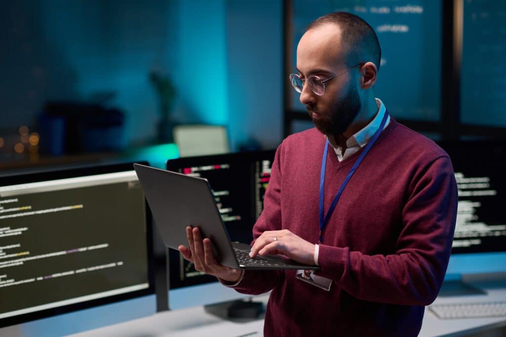 Homem em pé em escritorio com um notebook