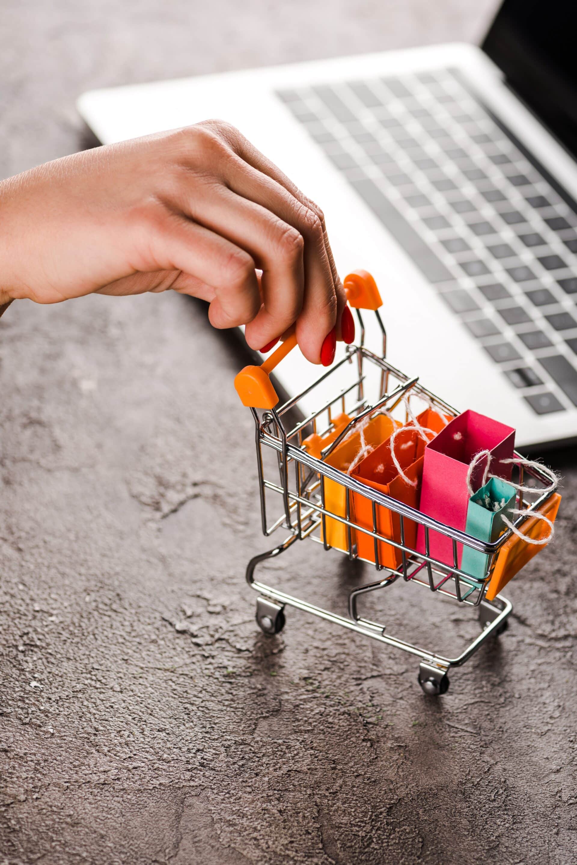 Carrinho de compras com sacolas, ao fundo um notebook