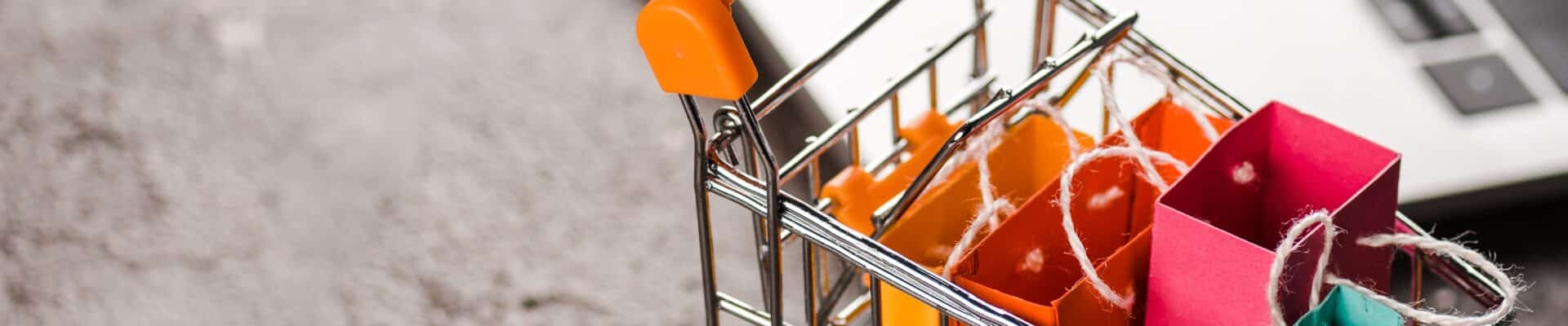 Carrinho de compras com sacolas, ao fundo um notebook