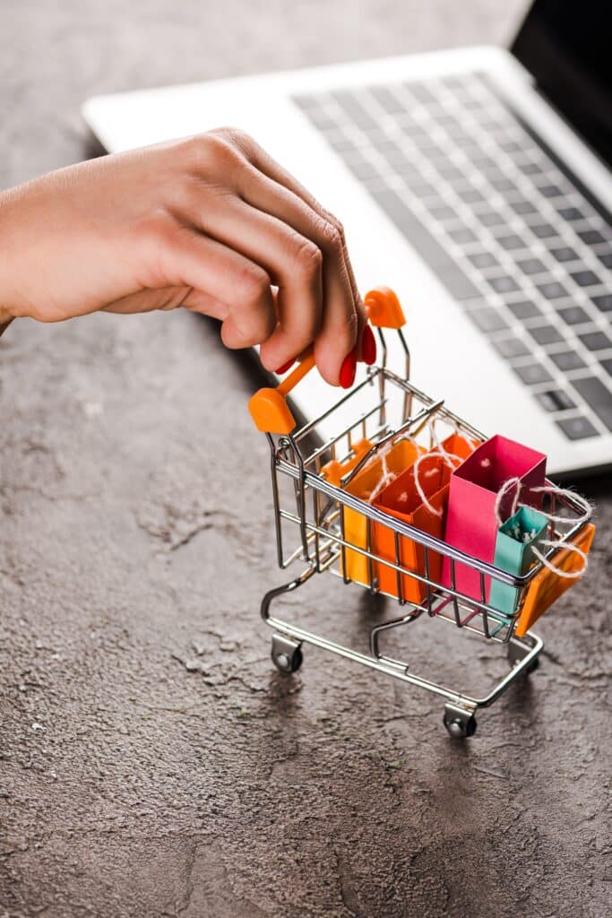 Carrinho de compras com sacolas, ao fundo um notebook