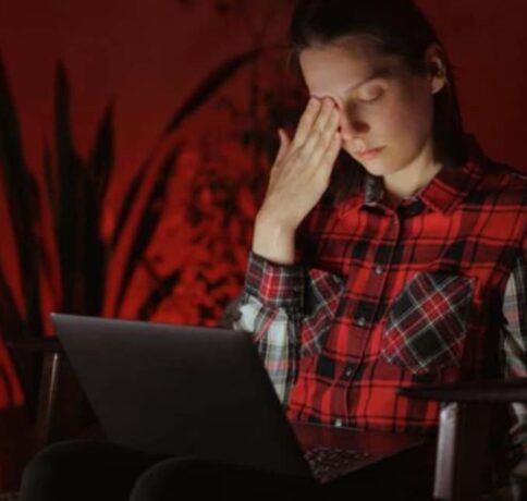uma mulher na fernte do notebook no escuro com cara de esgotada e preocupada
