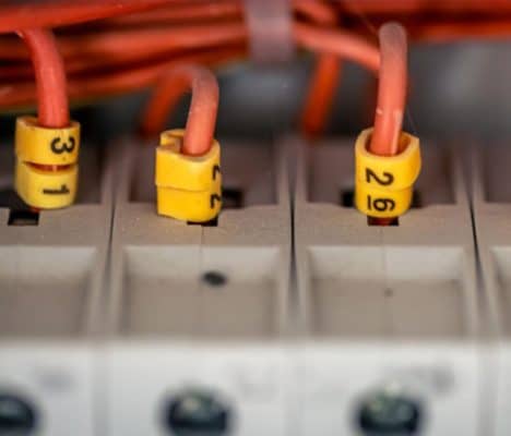 três cabos elétricos com isolamento vermelho inseridos em terminais de um bloco de conexão modular (régua de bornes) de cor bege