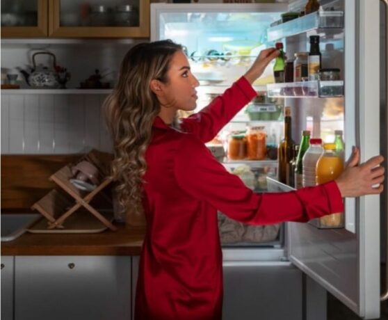 uma mulher de cabelo comprido e com blusa vermelha pegando alimentos na geladeira