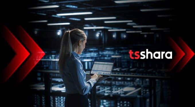Mulher de cabelo loiro preso, camisa social, de costas, trabalhando em um laptop em um centro de dados. A logo da TS Shara está ao lado, nas cores vermelho e branco