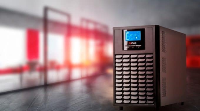um NOBREAK UPS SENNO VT 3KVA – MONO 220V da TS Shara em destaque sobre uma superfície lisa, com um ambiente corporativo desfocado ao fundo e iluminação avermelhada.