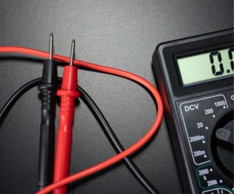 Detalhe aproximado de um multímetro digital e seus cabos de teste (ponta de prova) nas cores preto e vermelho.