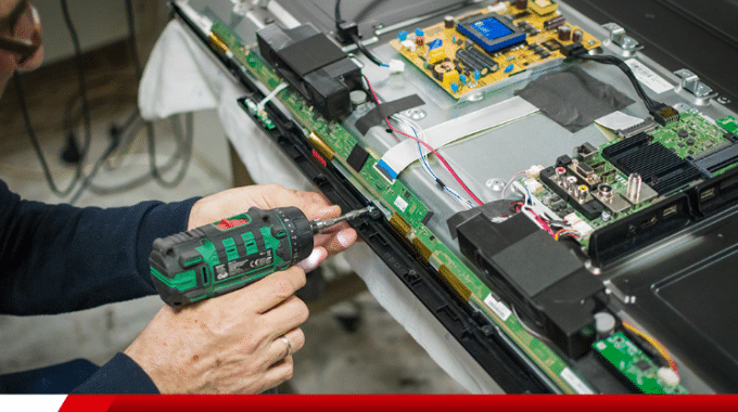 Um técnico, ou reparador, consertando a parte interna de uma televisão ou monitor. A pessoa está usando uma parafusadeira elétrica.