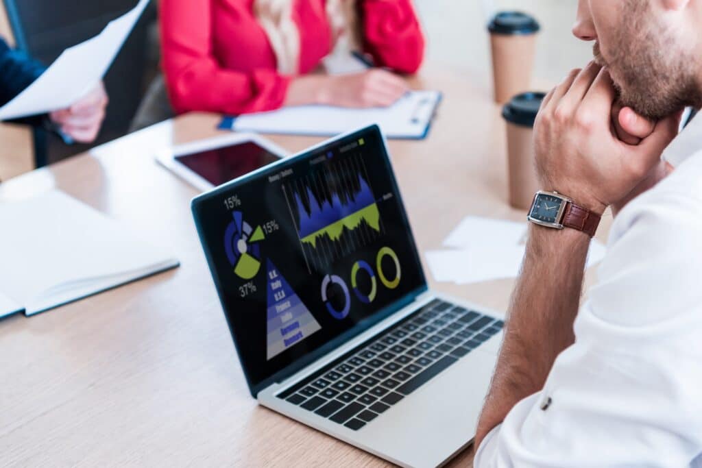 Uma visão parcial em close-up de um empresário em uma reunião, apoiando o queixo na mão com uma expressão pensativa.