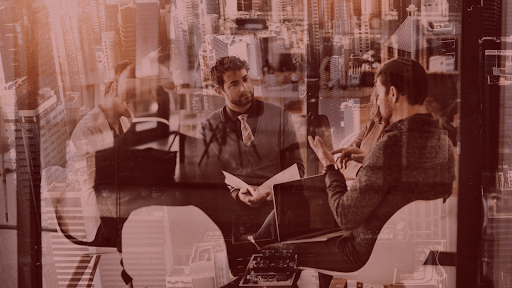 Grupo de profissionais em reunião corporativa dentro de sala de vidro com vista para a cidade