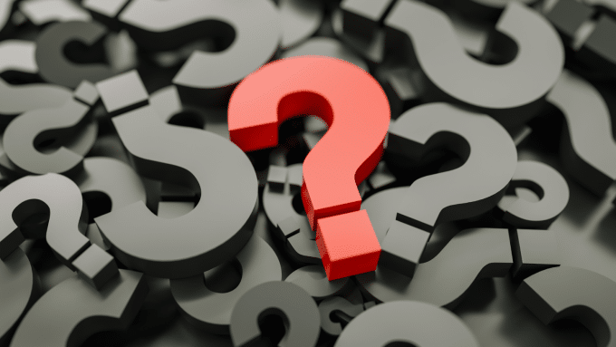 Imagem em 3D de uma pilha de pontos de interrogação em relevo. A maioria dos pontos de interrogação é de cor cinza-escuro. No centro, um ponto de interrogação em destaque, de cor vermelha.