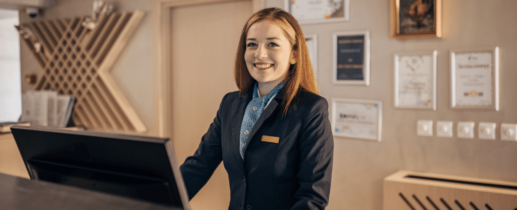uma recepcionista de hotel na cancada da recepção sorrindo
