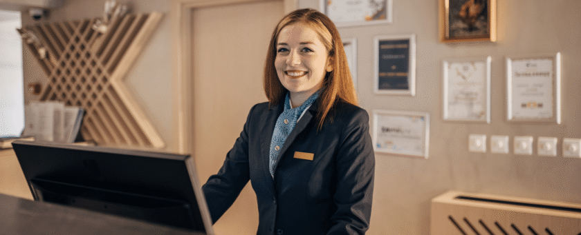 uma recepcionista de hotel na cancada da recepção sorrindo