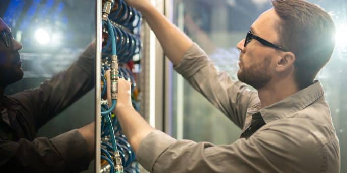 Um técnico ou profissional de TI, usando óculos escuros de segurança, trabalhando em um rack de servidor ou painel de telecomunicações.