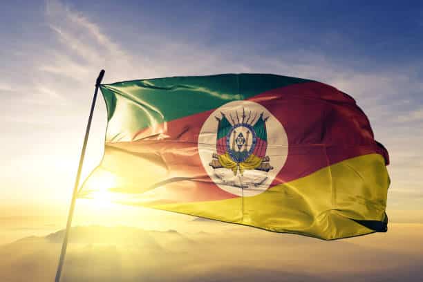 Uma imagem da bandeira do Rio Grande do Sul em um fundo de céu ensolarado