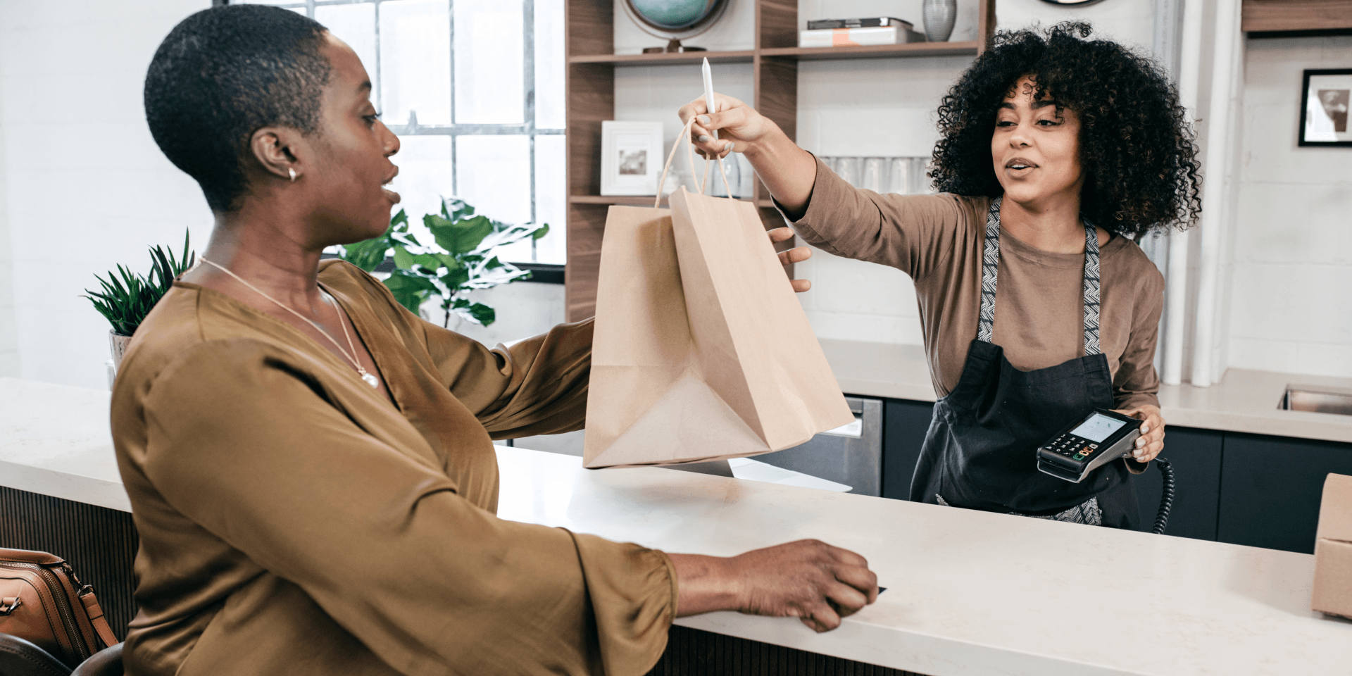 uma lojista no caixa da loja entregando sacolas para o consumidor