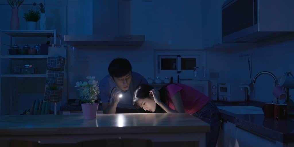 um homem e uma mulher em uma cozinha escura com uma lanterna procurando algo