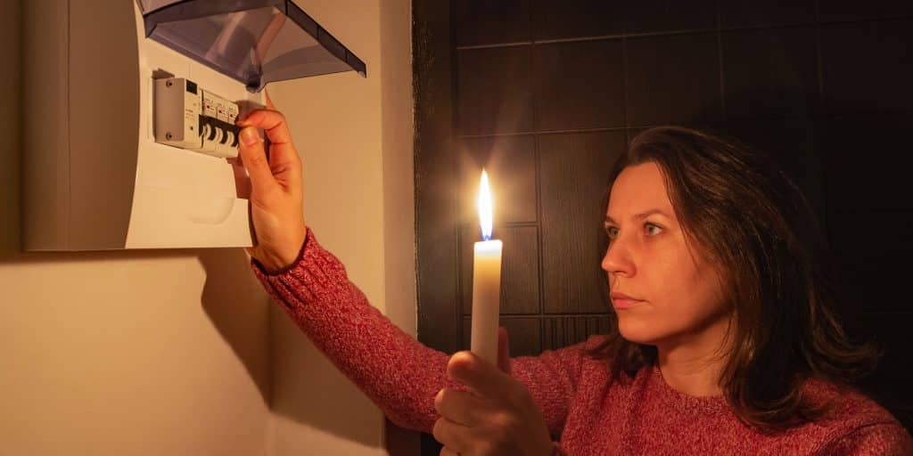 uma mulher segurando uma vela no escuro olhando a caixa de luz