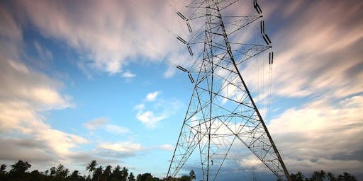 uma torre de energia elétrica no fundo com céu azul e algumas nuvens