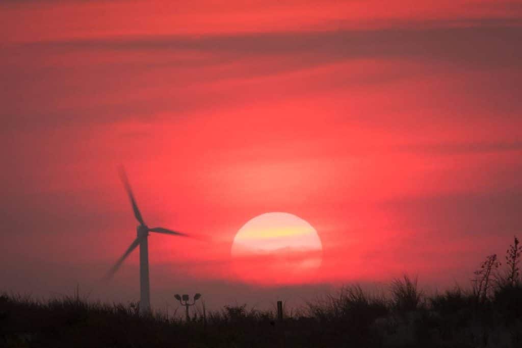 uma imagem de um por do sole e uma hélice de energia eólica