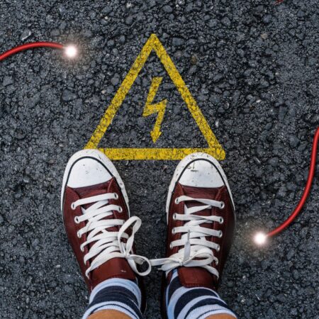 uma foto de dois pés com tênis all star vermelho na rua e um desenho no chão de alta voltagem