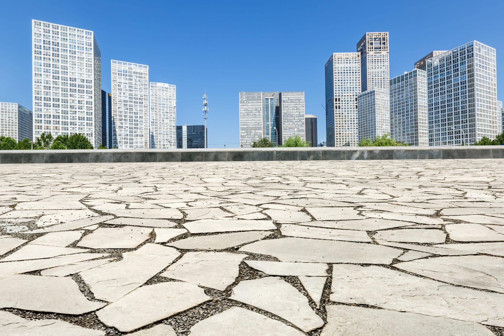 Uma vista de ângulo baixo de uma praça urbana pavimentada com pedras claras e irregulares em primeiro plano.