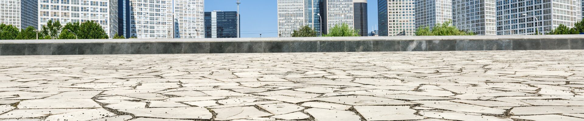 Uma vista de ângulo baixo de uma praça urbana pavimentada com pedras claras e irregulares em primeiro plano.