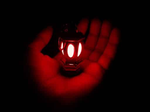 Uma mão segurando uma lanterna vermelha no escuro