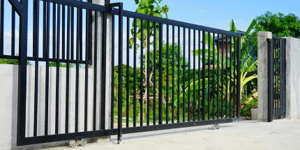 um portão automático preto e o fundo de dentro uma vegetação