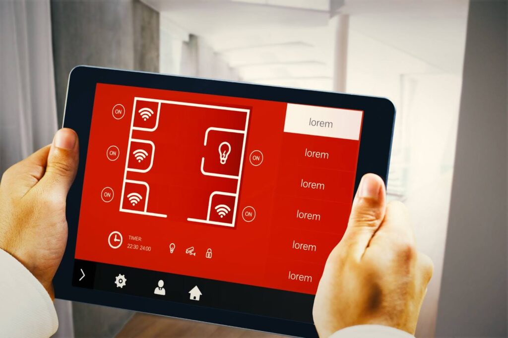 A primeira imagem exibe uma pessoa segurando um tablet horizontalmente. O dispositivo mostra um aplicativo de automação residencial com uma interface vermelha vibrante e ícones brancos. Na parte central, há um diagrama que representa a planta baixa de uma casa, dividida em quatro cômodos quadrados. Em cada um, há um ícone de Wi-Fi e um botão para ligar e desligar. No canto superior direito, há uma caixa de texto que diz "lorem", com várias linhas de texto de exemplo abaixo. Na parte inferior, uma linha de ícones simboliza as funções do sistema: relógio, configurações, um ícone de pessoa, uma casa e um cadeado.