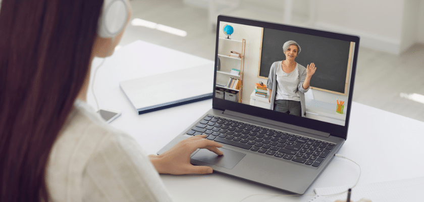 uma jovem estudando EAD e anotando esquanto escuta a professora falar no vídeo