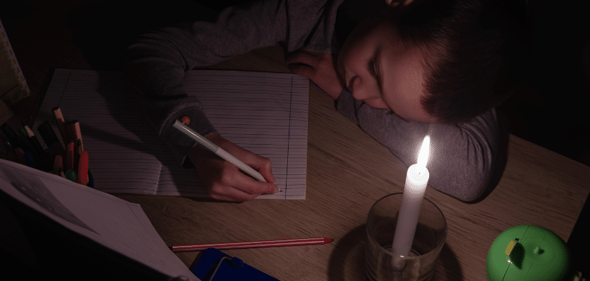 uma criança escrevendo em um caderno no escuro, sobre luz de vela