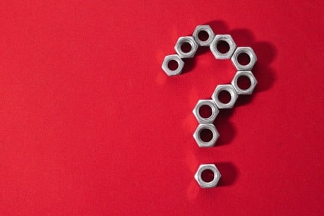 Um fundo vermelho com várias porcas metálicas de parafuso dispostas de forma a formar o desenho de um ponto de interrogação.