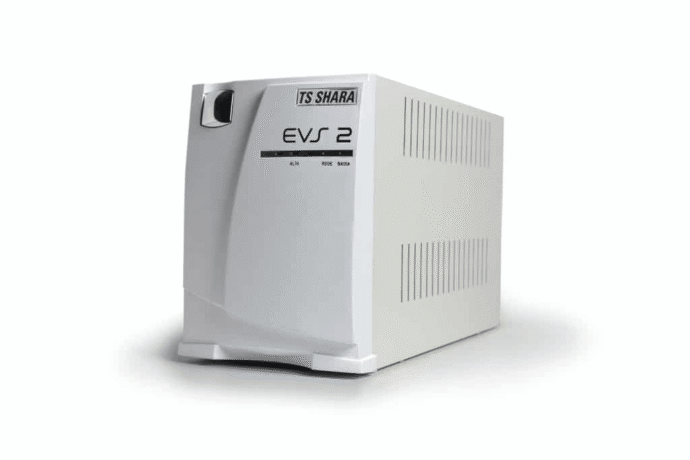 A imagem apresenta um nobreak TS Shara modelo EVS 2, que é um sistema de alimentação ininterrupta. O dispositivo tem um design branco, com um acabamento limpo e simples. O modelo possui entradas e saídas para fornecer energia de emergência, com uma tampa frontal que inclui a marca TS Shara e a inscrição "EVS 2". O nobreak é projetado para oferecer proteção contra falhas de energia, mantendo os dispositivos conectados operacionais durante quedas ou oscilações de energia.