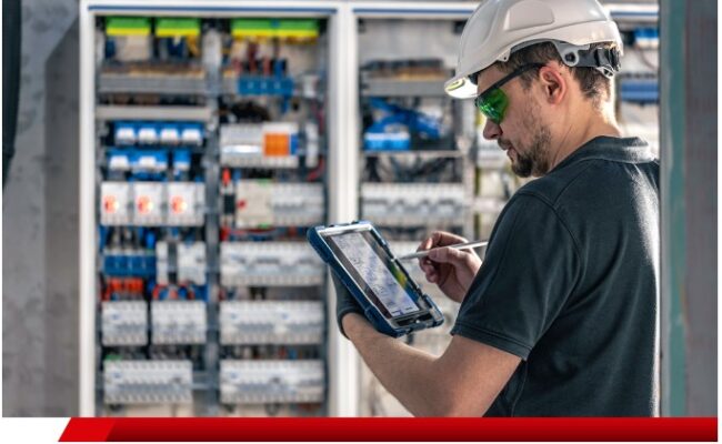 Técnico com capacete analisando painel elétrico usando tablet