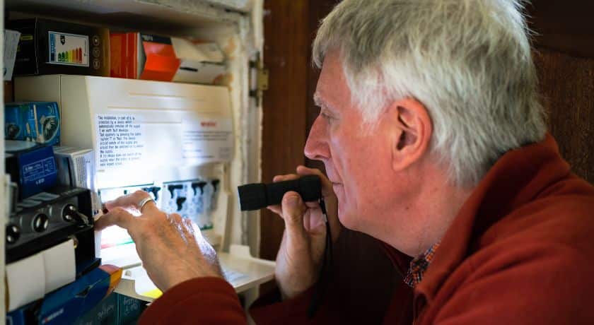 um senhor olhando acaixa de energia com uma lanterna