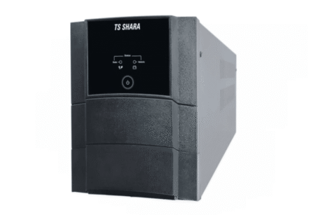 A imagem mostra um modelo de UPS (no-break) da marca TS SHARA. O aparelho é retangular e possui um acabamento em plástico de cor preta. Na parte frontal, há uma tela digital com ícones e botões de controle, que indicam o status do equipamento, como "On" e "Off". O design é robusto, com linhas simples e uma estrutura que se estende na parte inferior, sugerindo que o aparelho é de tamanho médio e feito para suportar equipamentos de médio porte.