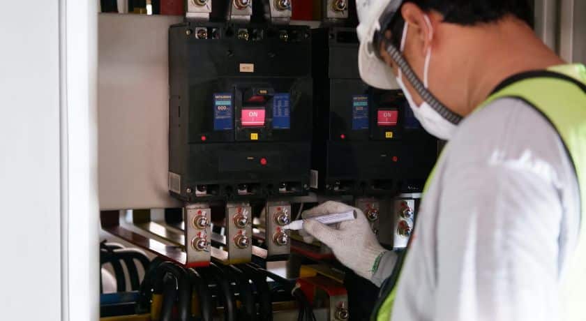 um eletricista equipado em frente a um quadro de energia fazendo manutenção