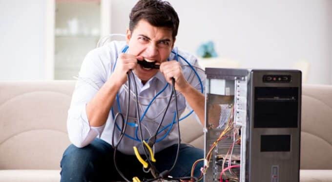 um homem agachado ao lado de uma CPU bravo e simulando que vai morder os fios 