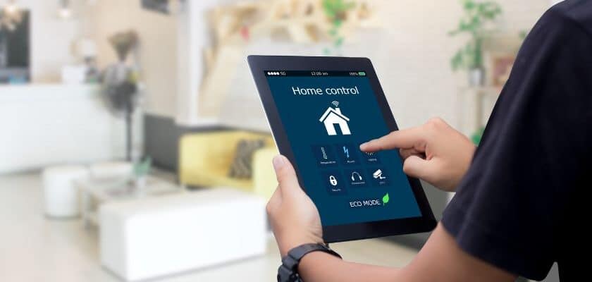 um rapaz segurando um tablet e clicando em um desenho de uma casa, fazendo referencia a automação e controle