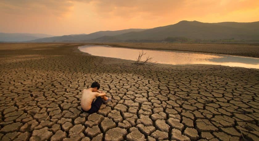 um menino sentado no chão em um rio seco olhando pro horizonte