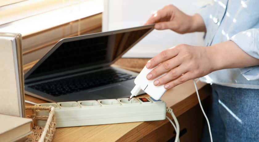 uma mão abrindo um notebook e conectando em uma extensão