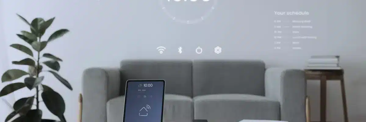 uma sala de estar com um sofá cinza, um vaso a esquerda com uma planta, uma mesa redonda amadeirada e um tablet em cima da mesa