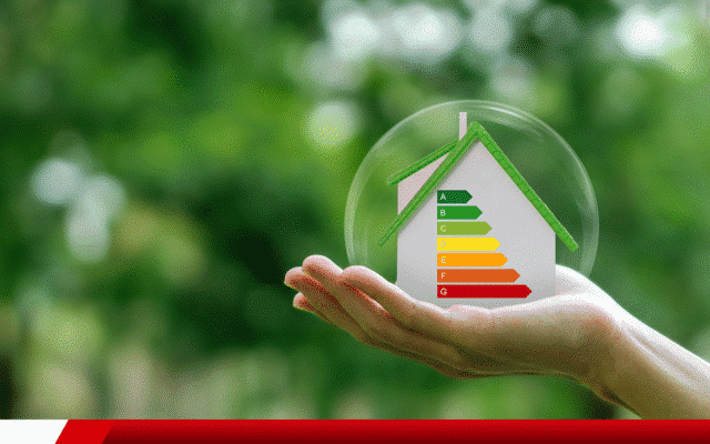 Mão segurando maquete de casa com etiqueta de eficiência energética em cores de A a G.