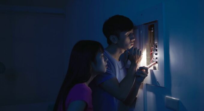 um rapaz e uma menina no escuro com um lanterna acesa olhando a caixa de registro de luz 